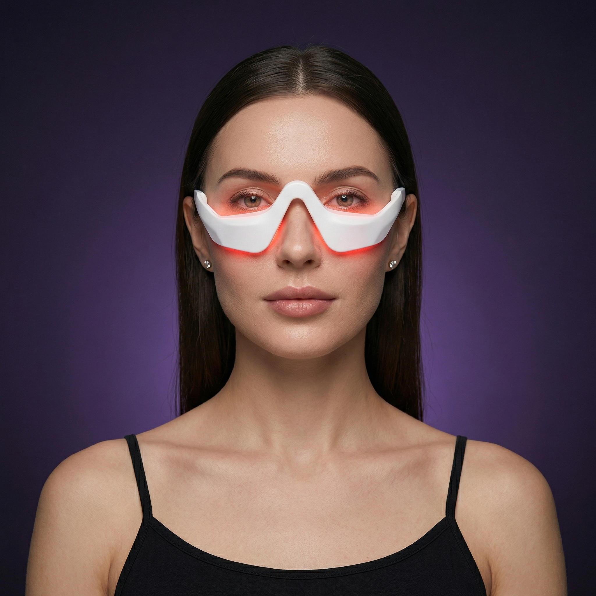 Studio portrait of a woman wearing the Ophelix Beauty LumiEye™ eye care device, featuring a sleek white design with a soft red LED glow around the under-eye area, set against a deep purple background.