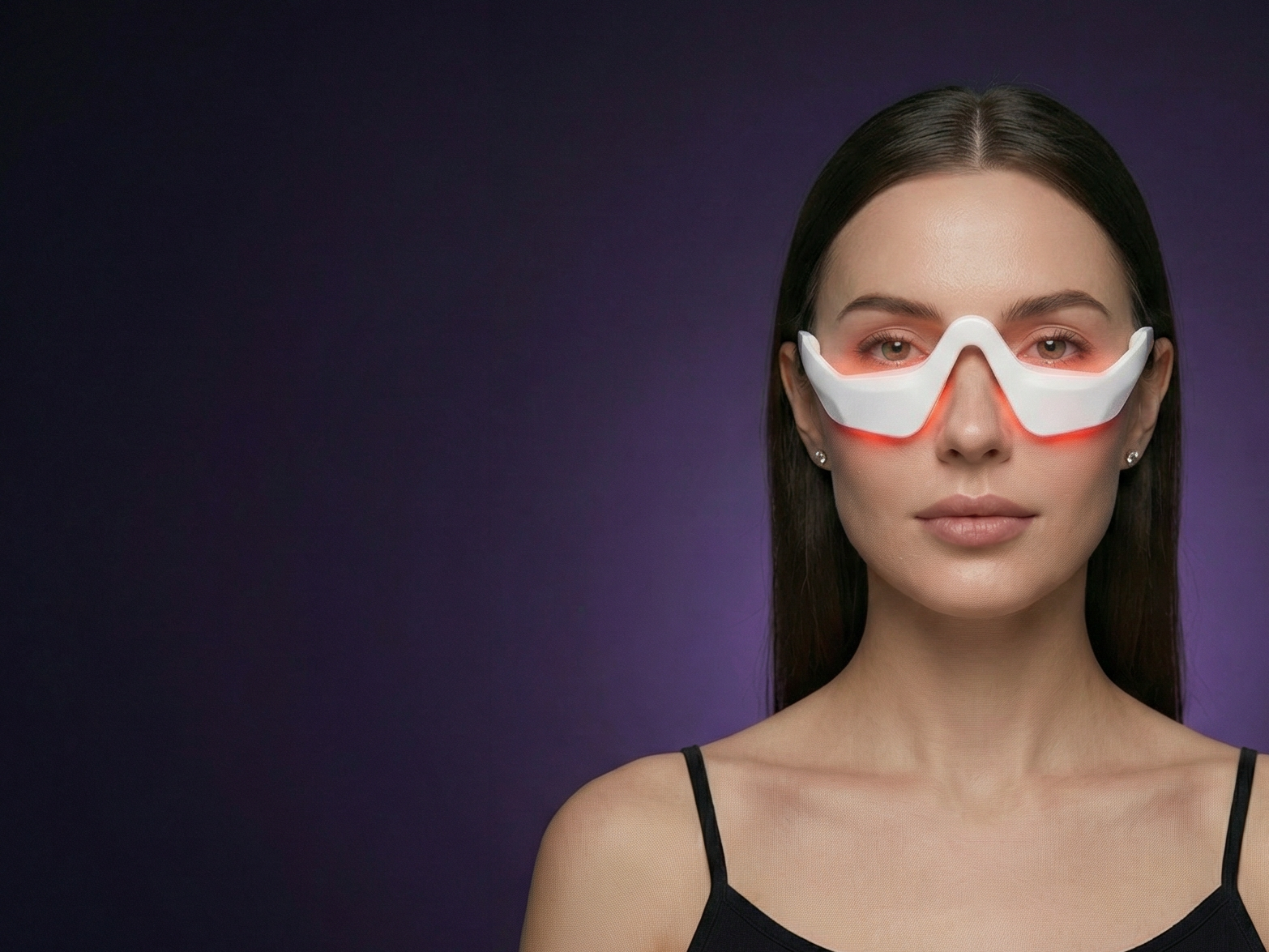 Studio portrait of a woman wearing the Ophelix Beauty LumiEye™ eye care device with soft red LED light around the under-eye area, set against a deep purple gradient background.